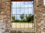 A wall and gates leading to a view. Behind the gates: a view of hope composed in greenery bushes and blue skies. 